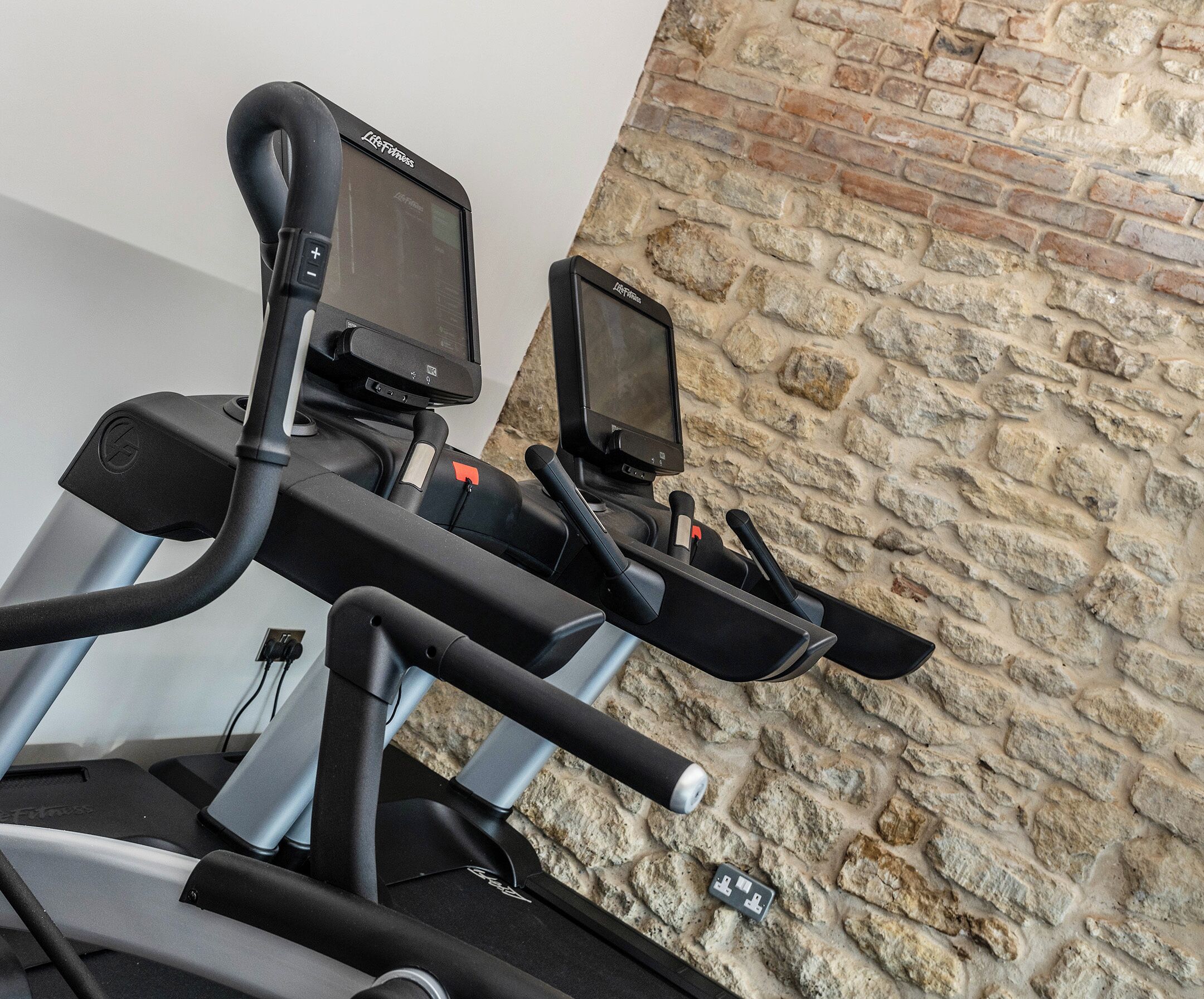 A stationary bike with a digital display and a control panel, set against a stone wall.