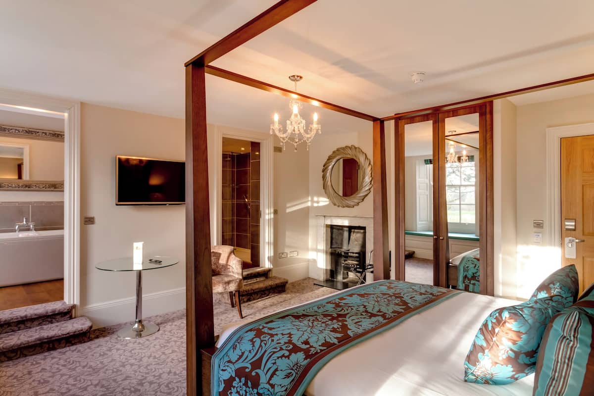 A bedroom with a large bed, a chandelier, a fireplace, and a television.