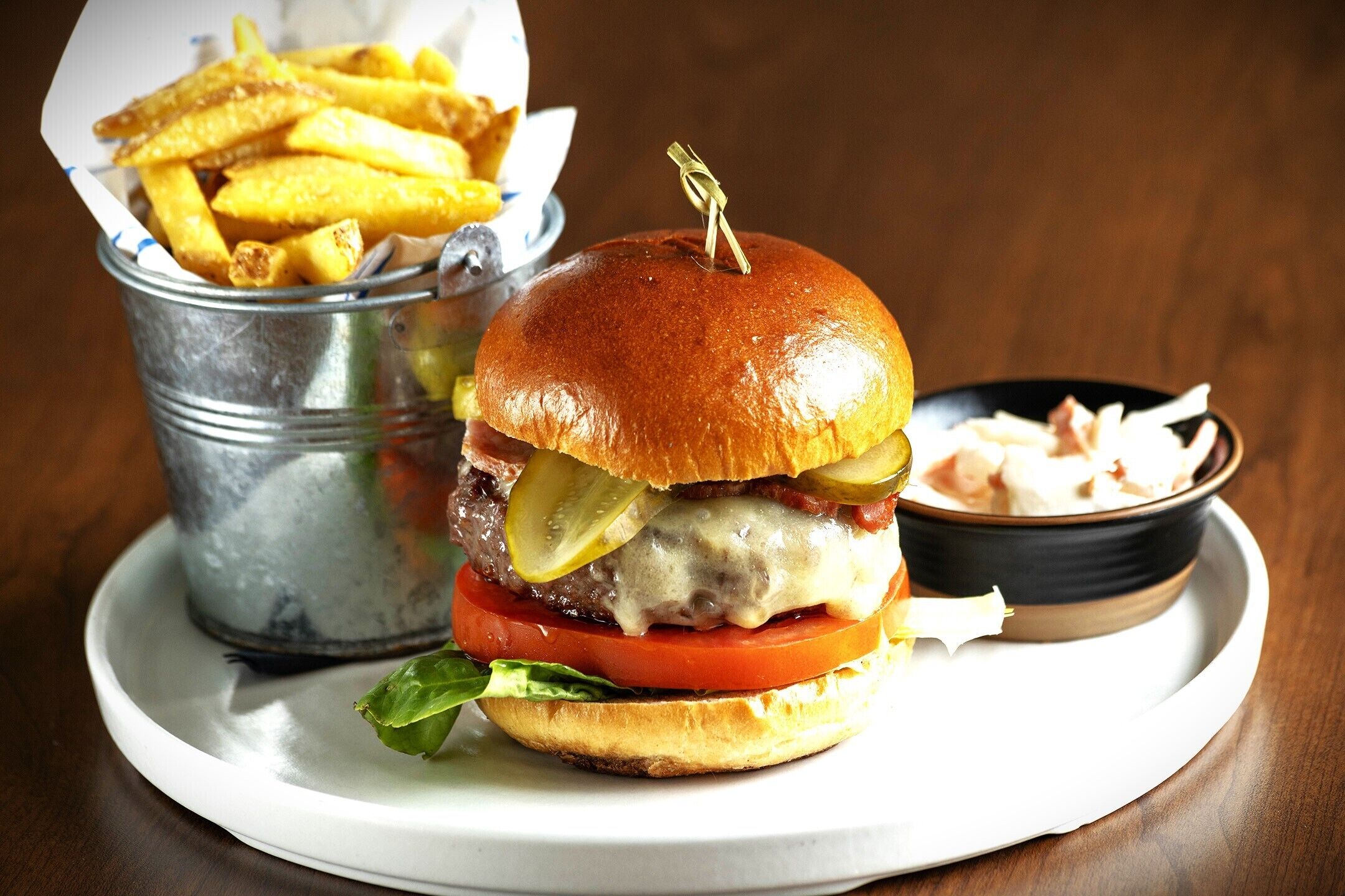 A burger with pickles, a side of fries, and a small bowl of coleslaw on a plate.