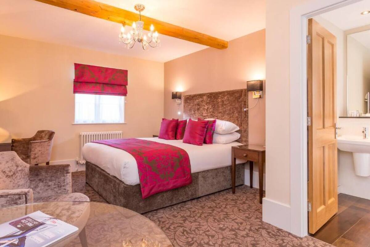 A bedroom with a large bed, a chandelier, a window with red curtains, a bedside table, and a nightstand.