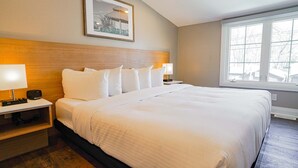 Habitación de hotel con una cama grande, dos mesitas de noche con lámparas, un cuadro enmarcado en la pared y una ventana con vistas a árboles.
