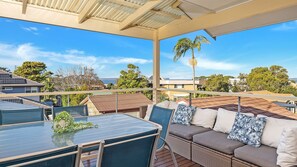 A balcony with a glass table and wicker sofa, overlooking a residential area with houses and trees. - Blue Horizon Vincentia (Vincentia)