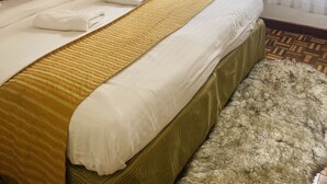 Une chambre d’hôtel avec un grand lit, une tête de lit, une table de chevet, un tapis moelleux et une fenêtre avec des rideaux légers.