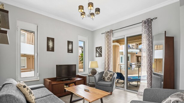 Una sala de estar moderna con sofá, sillón, mesa de centro, televisor y balcón con vista a la piscina.