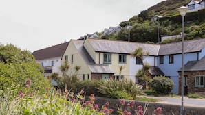 A row of houses with a stone wall in the foreground, a street lamp, and a hill in the background. - Kingsholm (Truro)