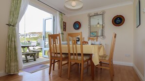 A dining area with a table set for four, wooden chairs, a ceiling light, and a view through a glass door to the outside. - Kingsholm (Truro)