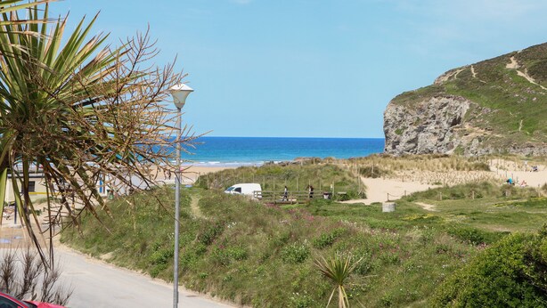 A coastal road with a lamp post, a white van, and a cliff with a path leading to the beach. - Kingsholm (Truro)