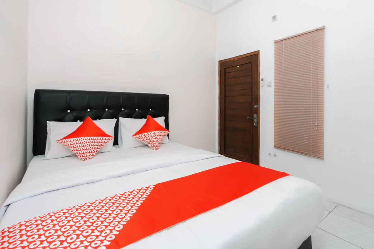 A neatly made bed with a black headboard, white bedding, and two red pillows.