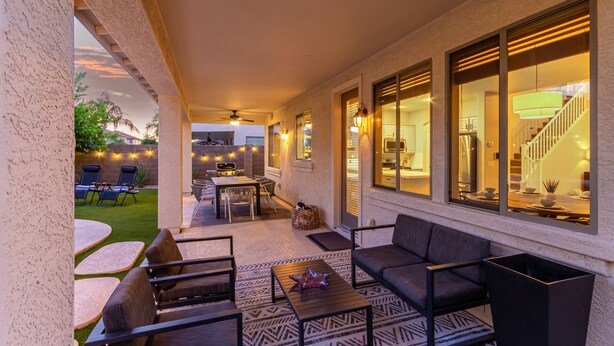 Un patio techado con mobiliario exterior, una parrilla y luces colgantes.