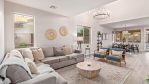 Una sala de estar amplia con un sofá gris, dos sillones, una mesa de centro y un comedor con una araña.