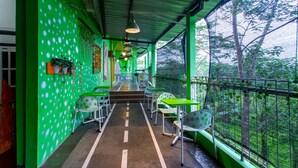 A covered outdoor seating area with green walls and white polka dot chairs, overlooking a forested area.