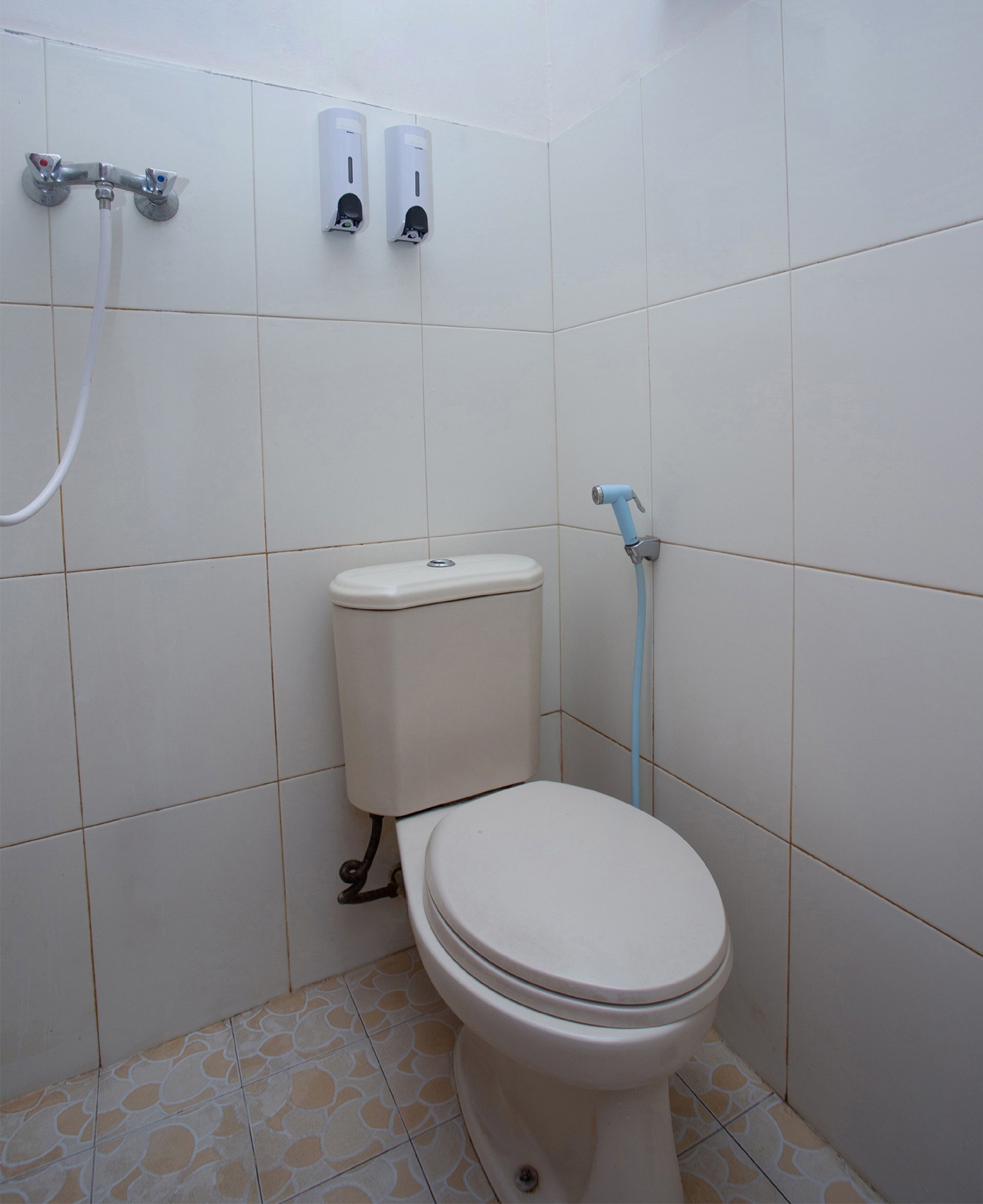 Ein kleines, sauberes Badezimmer mit Toilette, einem Händetrockner und einem Duschkopf.