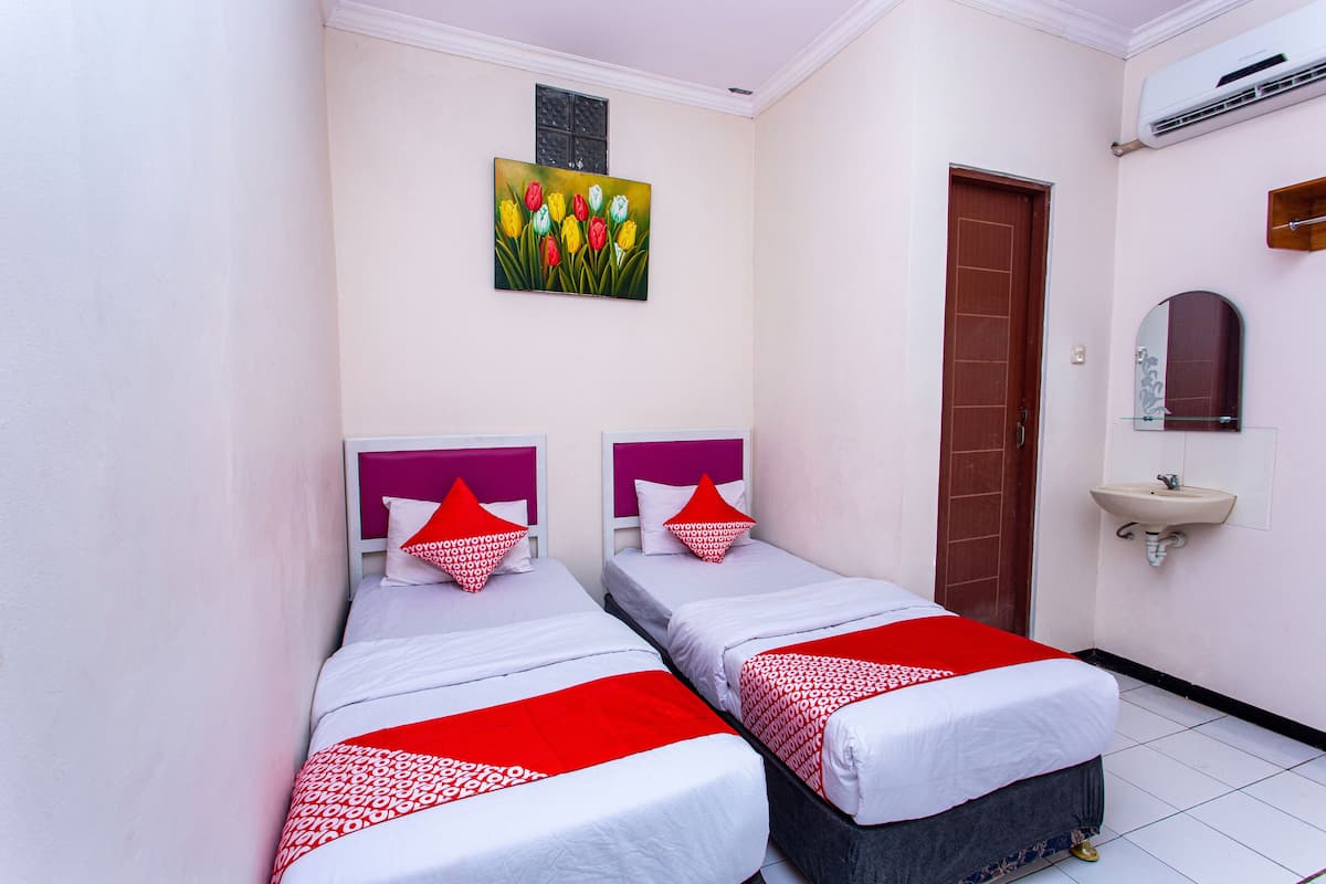 Ein Hotelzimmer mit zwei Betten, einem Blumenbild an der Wand, einer Tür, einem Waschbecken und einer Klimaanlage.