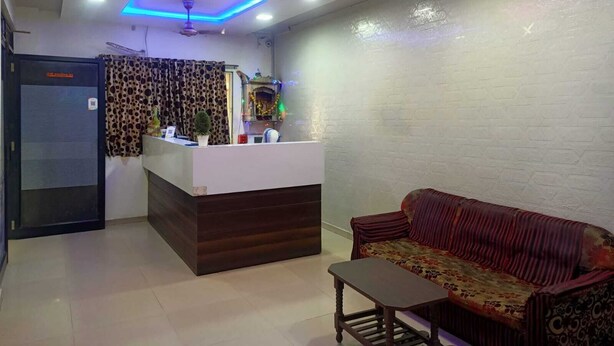 A reception area with a wooden reception desk, a sofa, and a small table. - Hotel Silver Inn - Naroda (Ahmedabad)