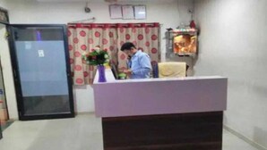 A reception area with a desk, a potted plant, a curtain with a polka dot pattern, and a wall-mounted shelf with items. - Hotel Silver Inn - Naroda (Ahmedabad)