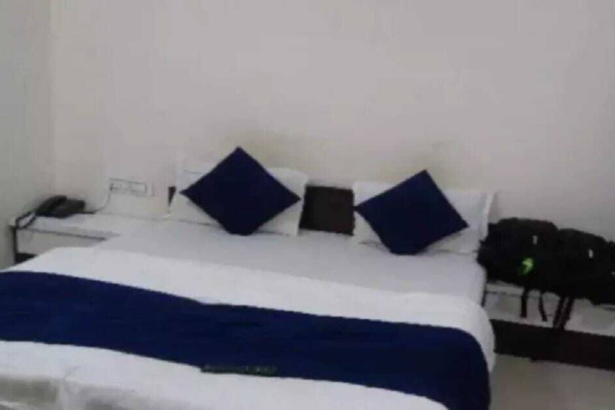 Quarto de hotel com uma cama, travesseiros, cobertor, telefone e uma mochila.