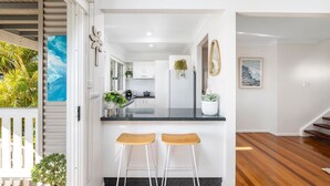 A modern kitchen with white cabinetry, a black countertop, and two wooden bar stools. - Cabane Sur Mer – views of Shoal Bay (Shoal Bay)