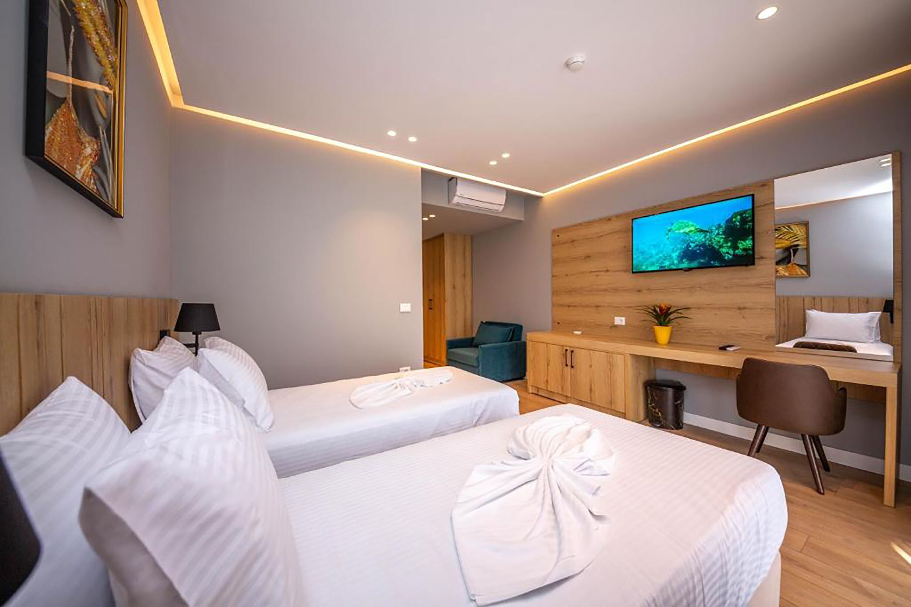 A hotel room with two beds, a desk, a TV, and a wooden wall.