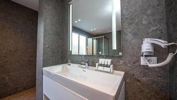 A modern bathroom with a large white sink, a mirror, and a hairdryer mounted on the wall.