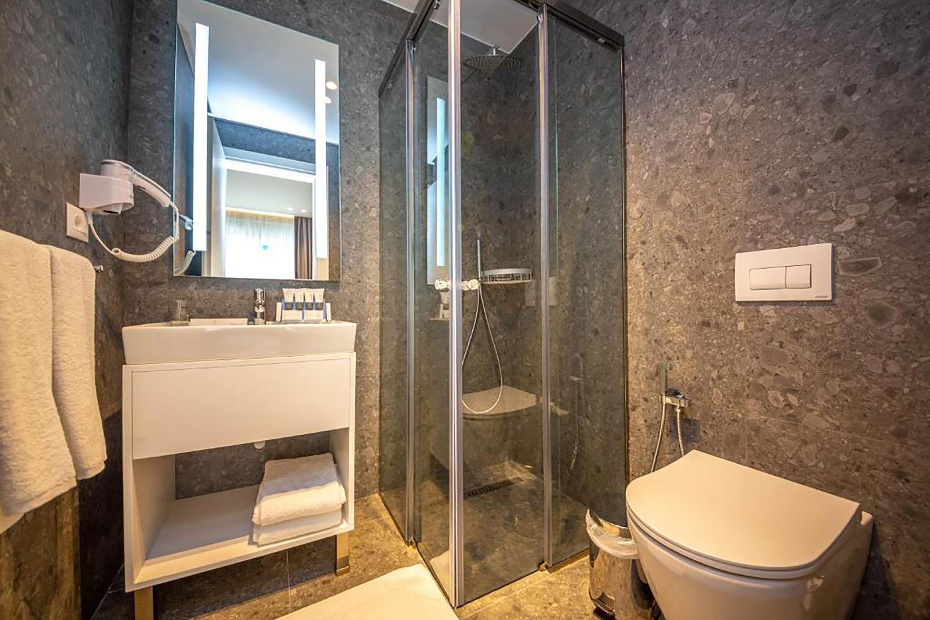A modern bathroom with a glass-enclosed shower, a white sink, and a toilet.