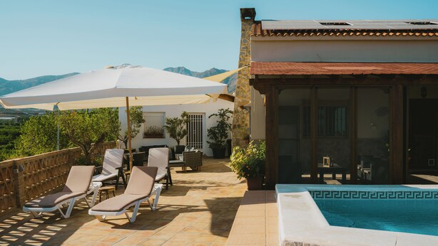 A pool area with lounge chairs and a large umbrella, surrounded by a stone wall and a view of mountains. - Rural House on the Tropical Coast with Salt Pool (Salobreña)