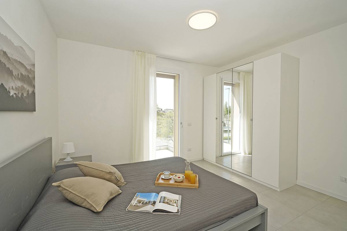 A bedroom with a bed, a bedside table with a lamp, a tray with breakfast items, and a large mirror.