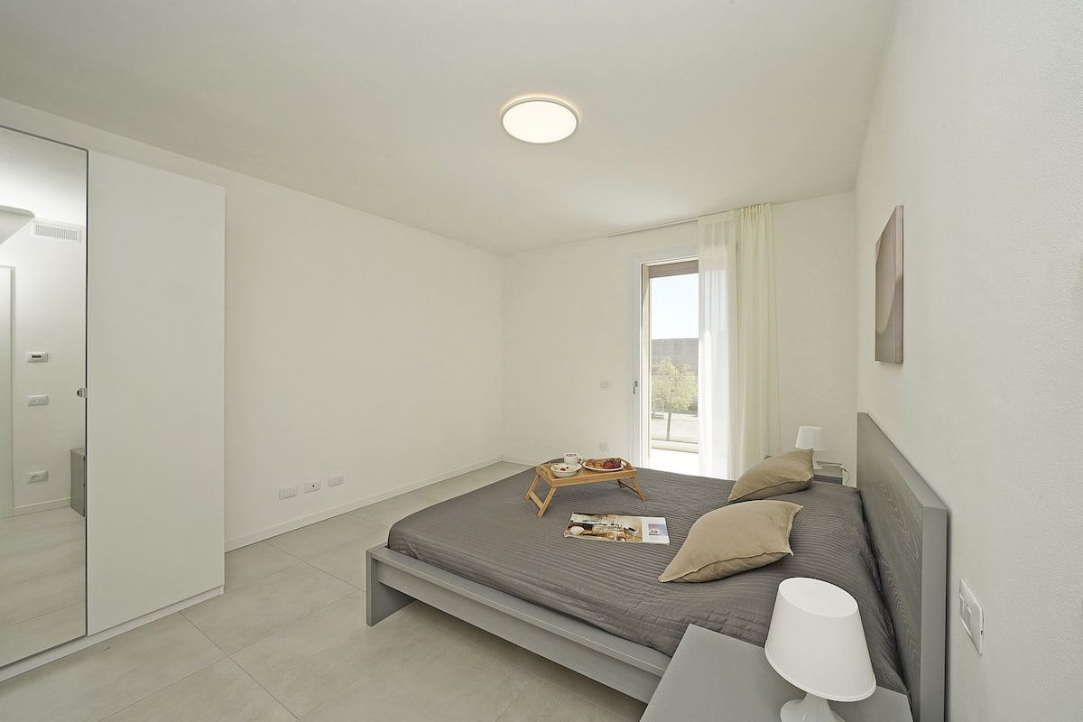 A bedroom with a bed, bedside table, lamp, and a window with curtains.