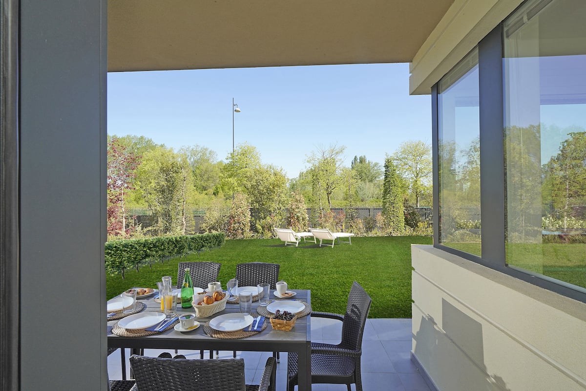 An outdoor dining area with a table set for a meal, surrounded by chairs, and a view of a well-maintained garden and lawn.