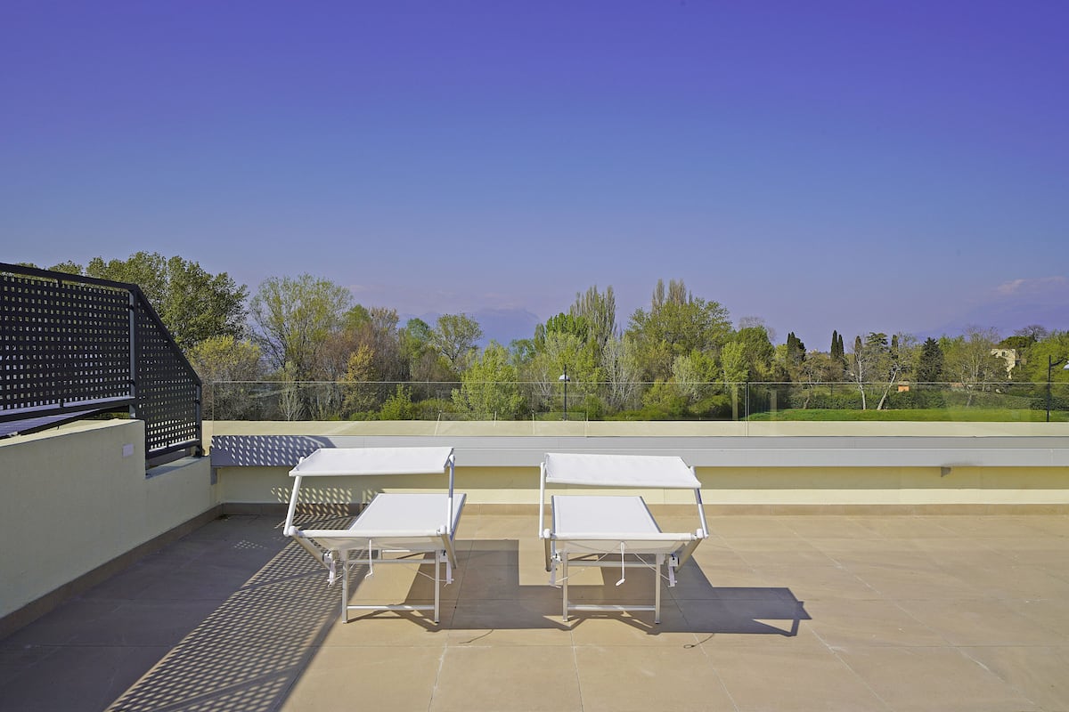 A rooftop terrace with two white sun loungers and a metal railing.