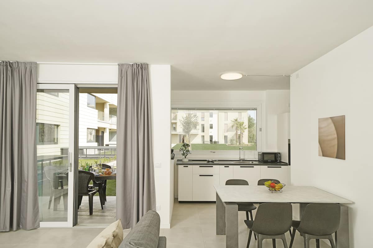 A modern apartment with a dining area, kitchenette, and a balcony with curtains.