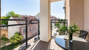 Un balcon avec une table et une chaise en verre, un vase rempli de fleurs et une vue sur les immeubles et les voitures en contrebas.