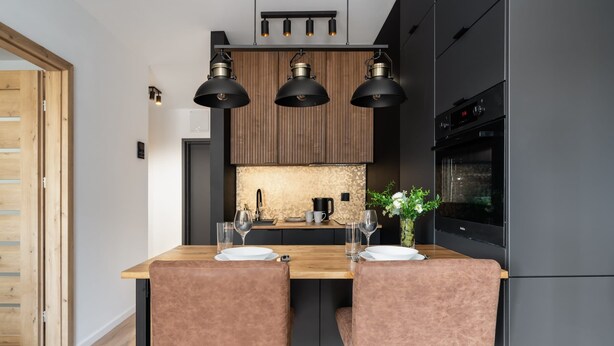Une cuisine moderne avec un îlot central en bois, des suspensions noires et un four encastré.