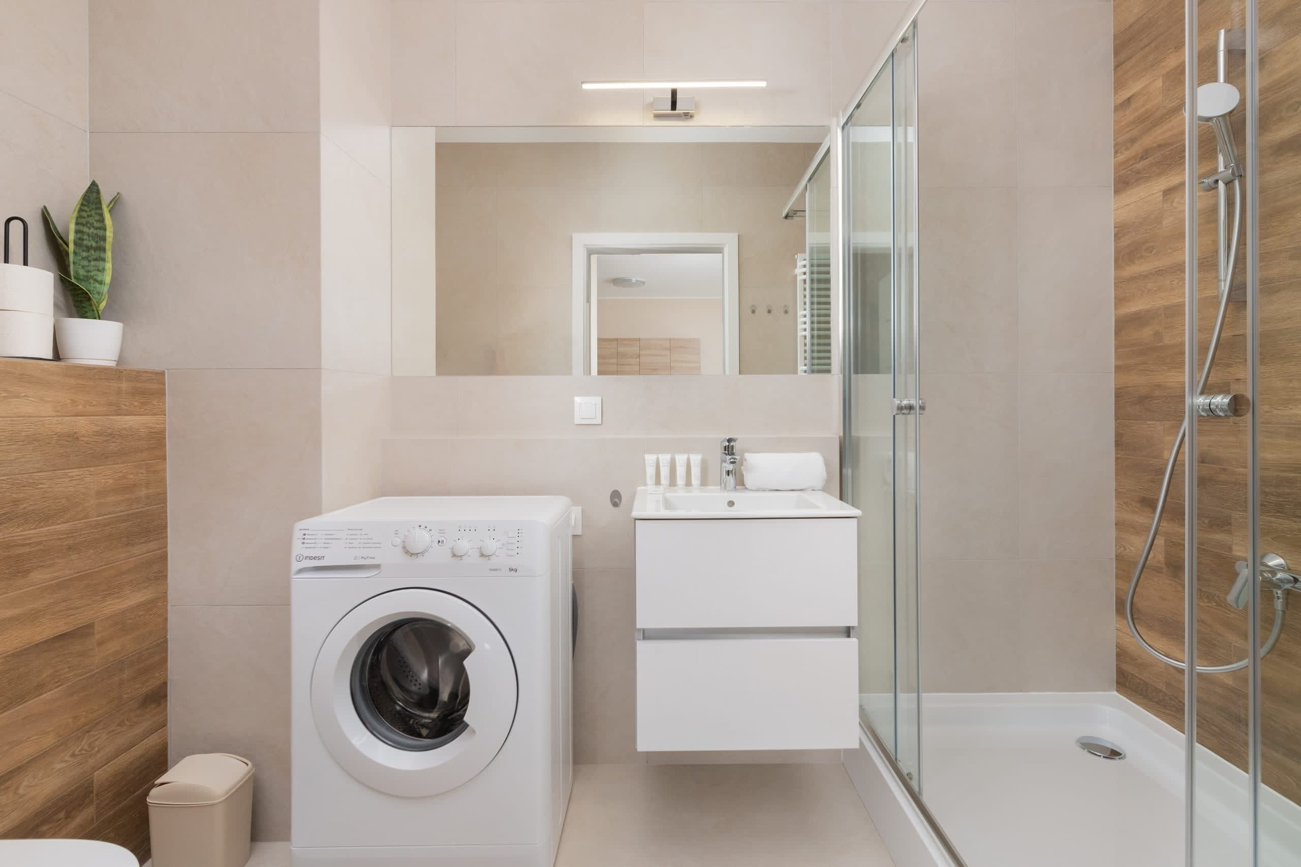 Une salle de bain moderne équipée d’un lave-linge, d’un évier et d’une douche à parois de verre.
