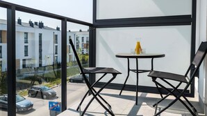 A balcony with a glass door, two black folding chairs, a small round table, and a glass of orange juice. - Elegant Apartment in Gdynia | Balcony and Private Parking (Gdynia)