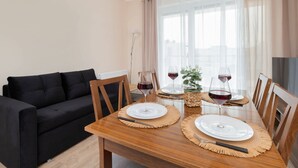 A dining area with a wooden table set for two, two wine glasses, and a potted plant. - Elegant Apartment in Gdynia | Balcony and Private Parking (Gdynia)