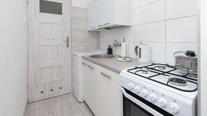 Une cuisine de taille réduite, avec un poêle, un évier et des placards blancs.