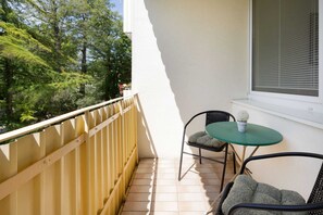 Un balcone con ringhiera gialla, due sedie, un tavolino e una pianta in vaso.