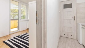 Un couloir doté d’un plancher en bois, d’un tapis à rayures noires et blanches, d’une porte blanche avec une petite fenêtre et d’un radiateur.