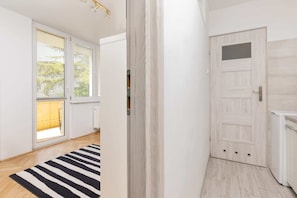 A hallway with a wooden floor, a black and white striped rug, a white door with a small window, and a radiator.
