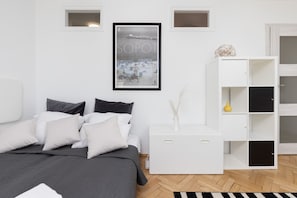 A modern bedroom with a bed, white nightstands, a framed picture, and a white shelving unit.