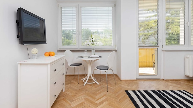 Une petite pièce lumineuse, avec un bureau blanc, deux chaises, un téléviseur et de grandes fenêtres.