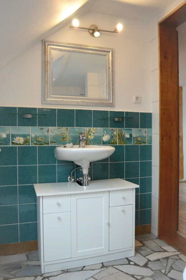 Un baño con un lavabo blanco, azulejos verde mar, un espejo y una puerta de madera.