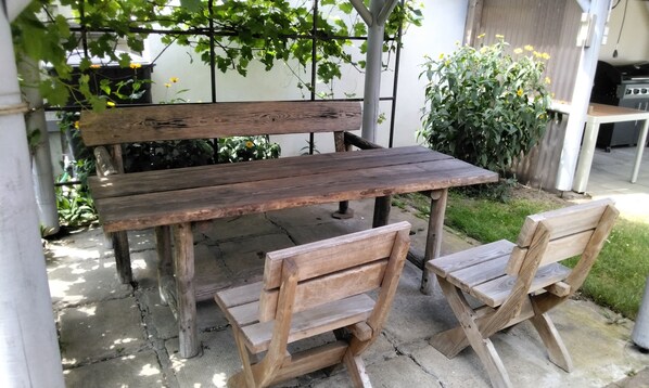 A wooden outdoor table with benches, surrounded by greenery and a garden.