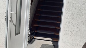 A white door with a small window, leading to a staircase with wooden steps and a metal handrail. - Charming guest house by the lake<br> (Bad Saarow)