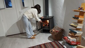 A room with a wood-burning stove, a bookshelf with books, and a woven basket on the floor. - Refúgio no Campo. A tranquilidade tão próxima da cidade, no coração do Alentejo. (Évora)