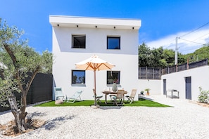 A modern two-story building with a white exterior, a patio with a table and chairs, and a large umbrella. - Maison Coquette (Nice)