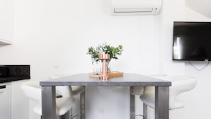 A modern kitchen with a marble countertop, two white bar stools, and a potted plant on the table.