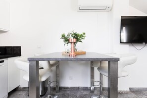 A modern kitchen with a marble countertop, two white bar stools, and a potted plant on the table. - Maison Coquette (Nice)