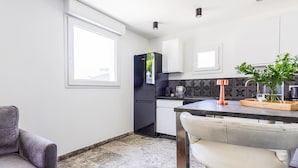 A modern kitchen with white cabinets, a black refrigerator, and a dining area with a white chair and table.