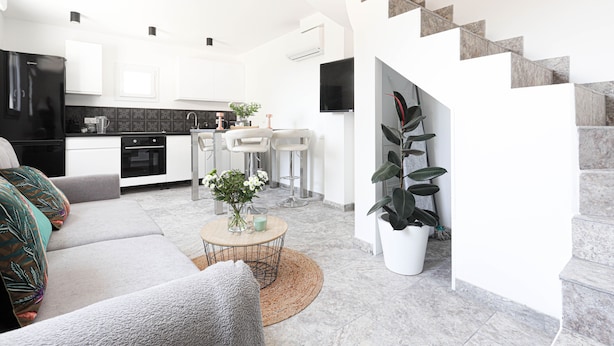A modern living room with a sofa, coffee table, and a kitchen area with white cabinets and a black countertop.